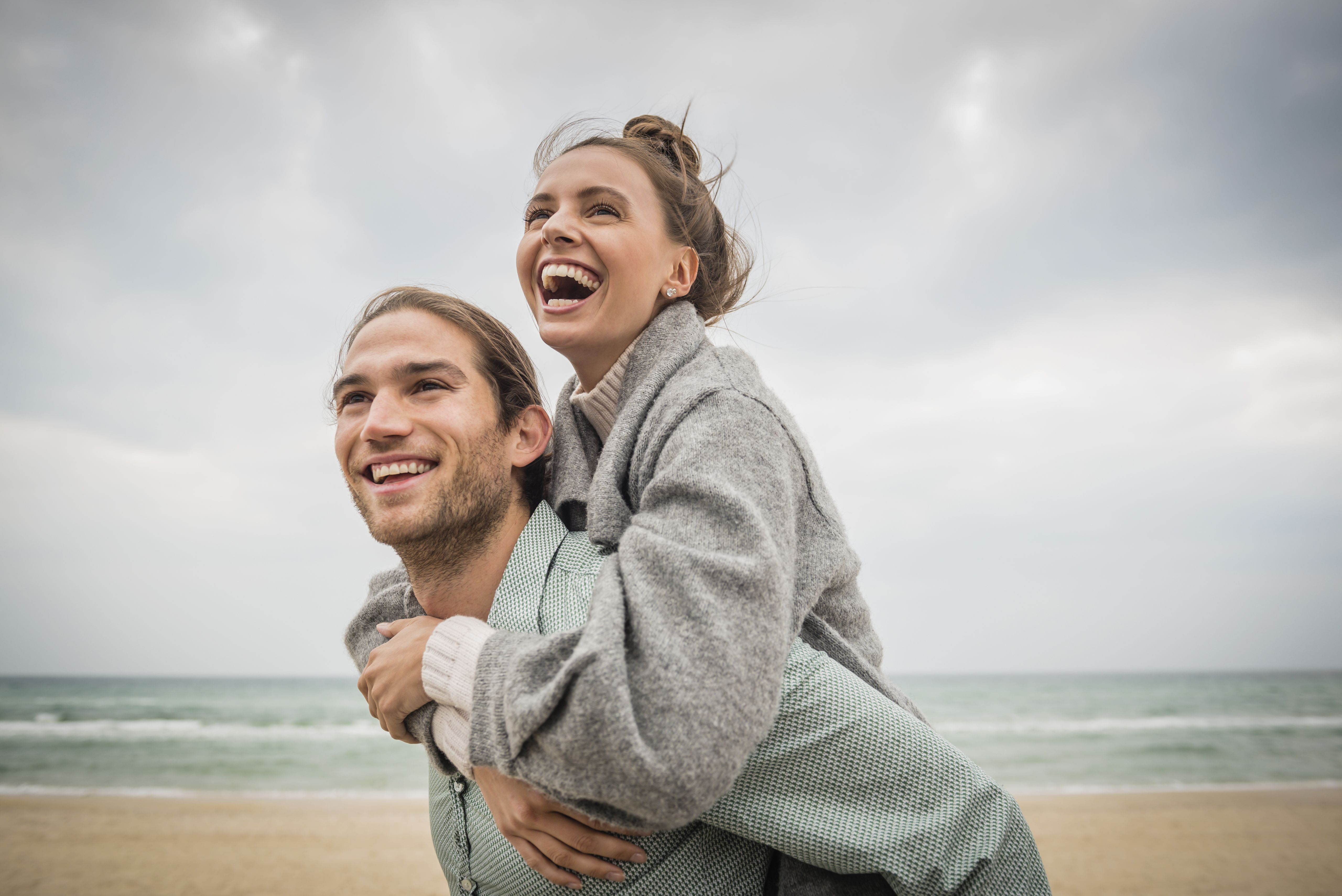 Coppia giovane e felice su una spiaggia soleggiata, con l'uomo che porta la donna sulla schiena, a illustrare un incontro serio, una relazione duratura e momenti di complicità