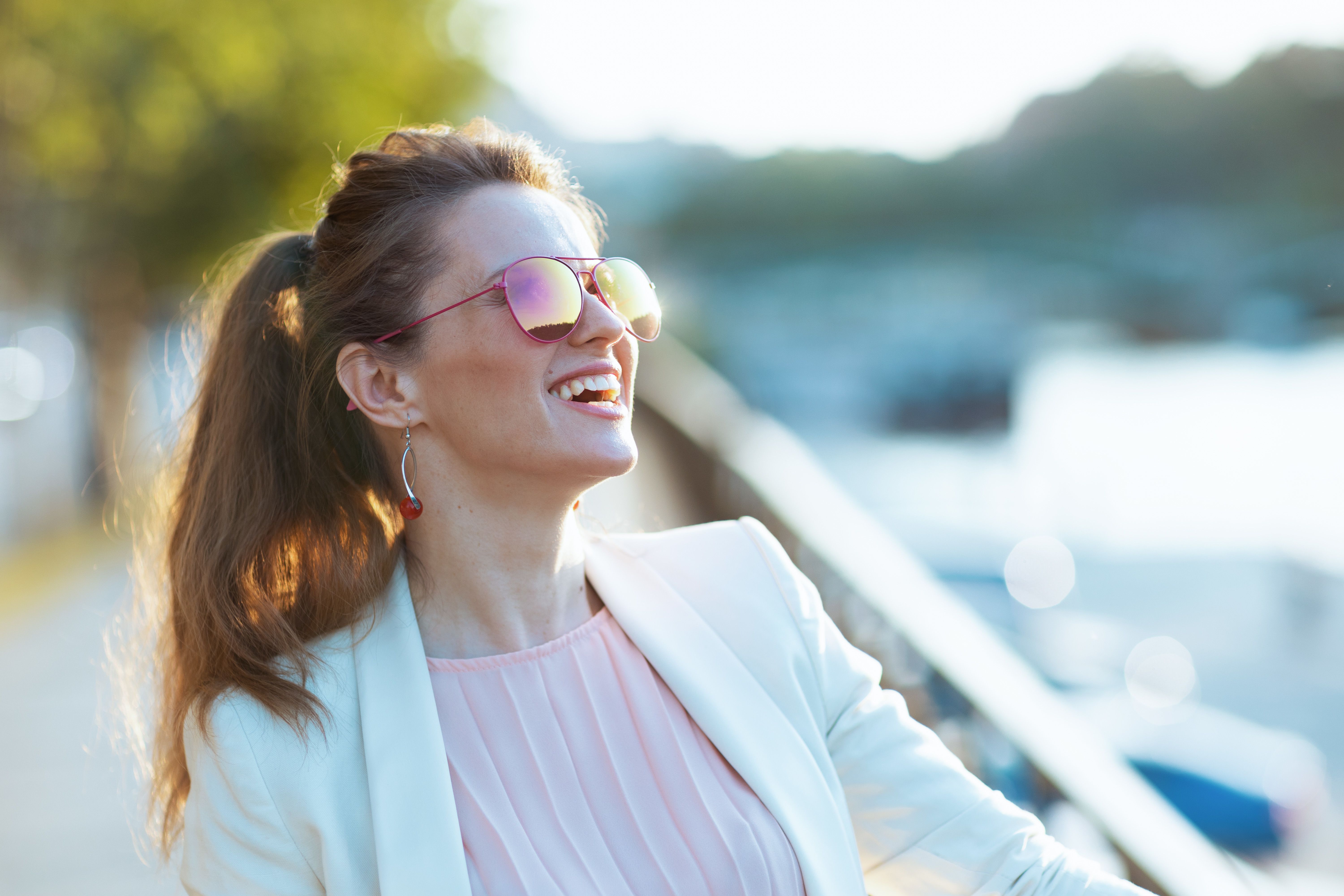 Giovane donna sorridente con occhiali da sole, seduta a un tavolino all’aperto in attesa del suo primo appuntamento dopo un incontro su un sito di incontri serio.