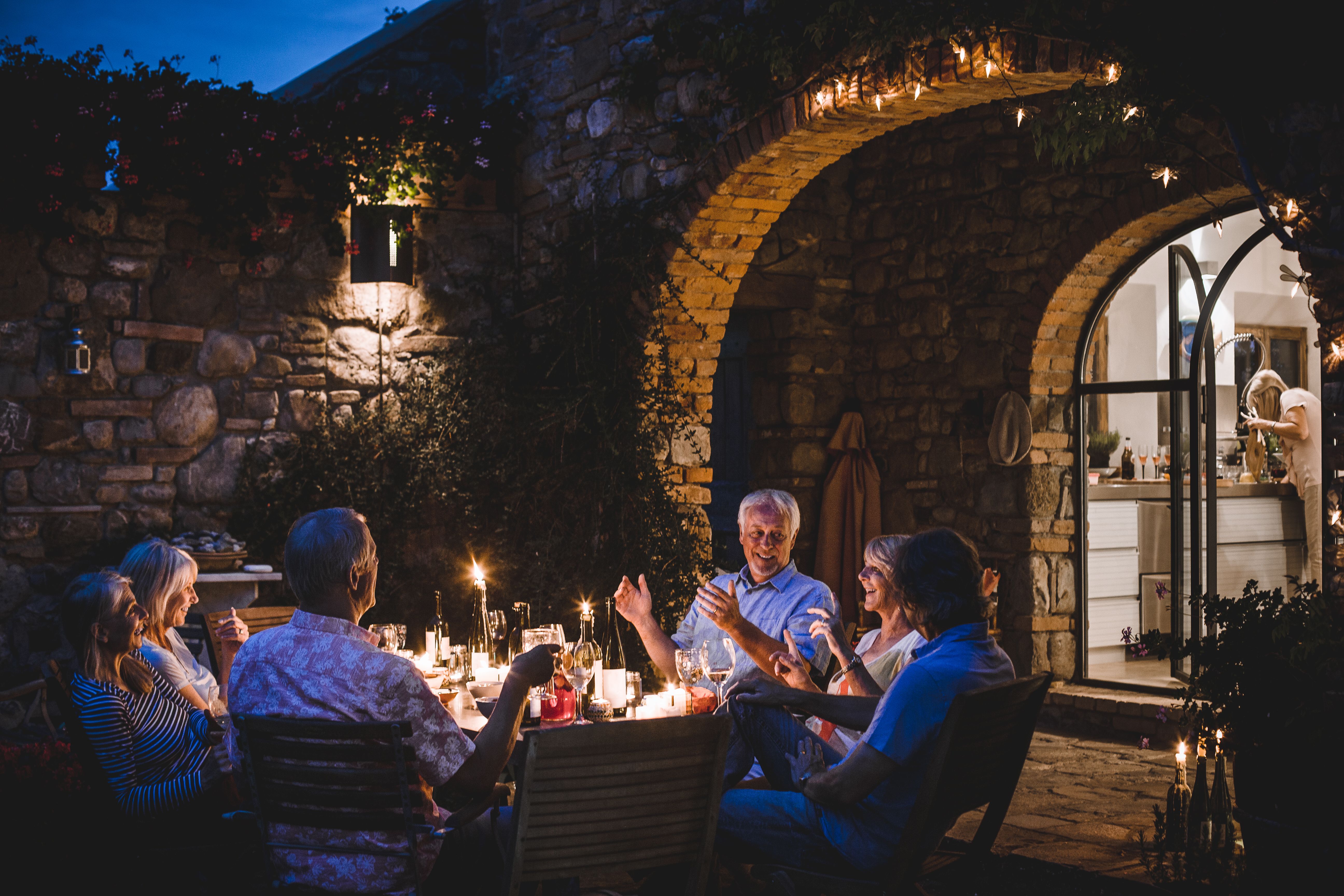 Gruppo di amici sorridenti che condividono una cena in un giardino di sera, a illustrare un nuovo inizio, incontri autentici e la ripresa della vita sociale dopo un divorzio.