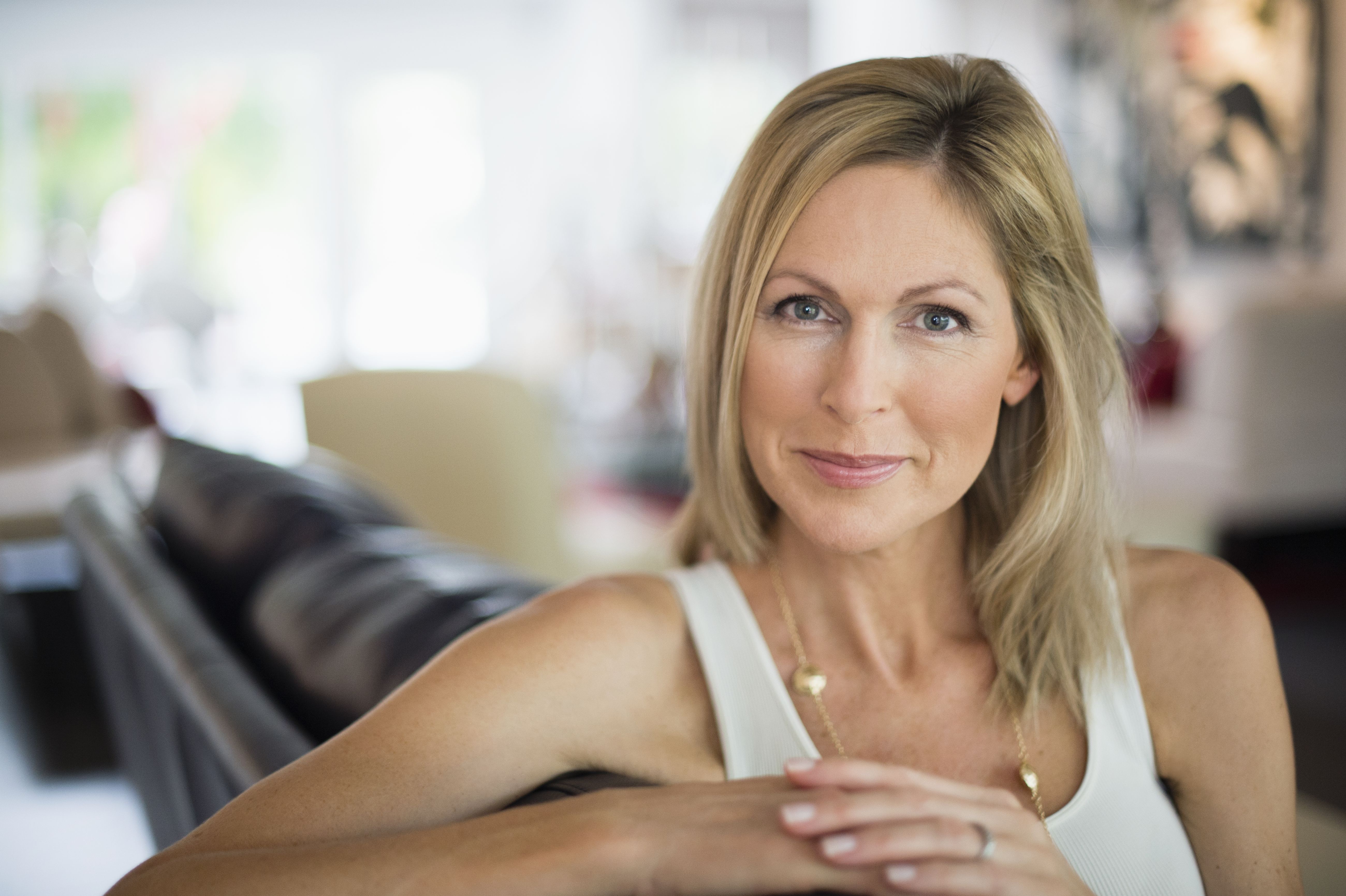 Donna over 40 seduta nel suo salotto, che guarda l'obiettivo con sicurezza, a illustrare un nuovo inizio e la ricerca di una relazione seria dopo un divorzio.