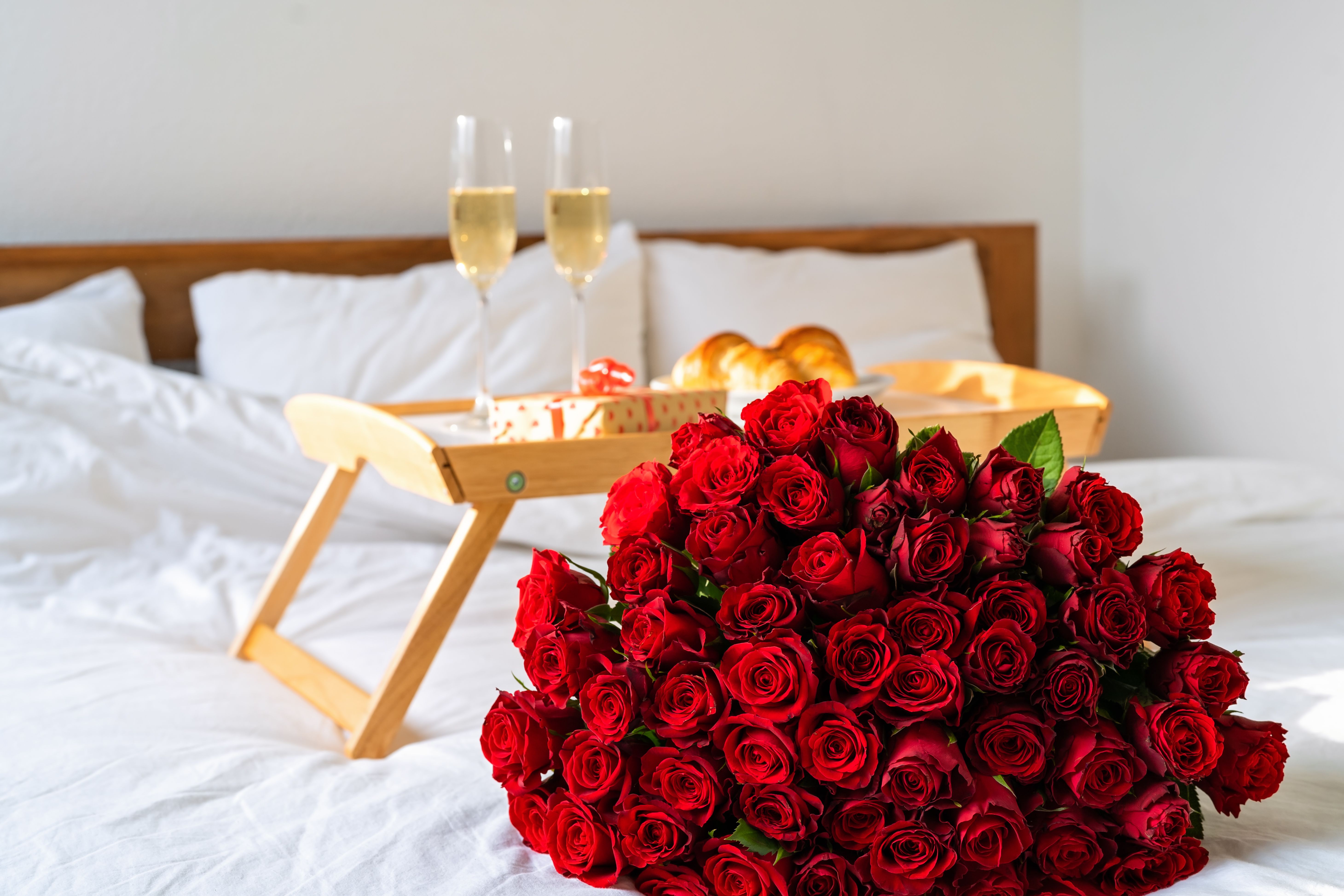 Grande mazzo di rose rosse su un letto accanto a una colazione per due.