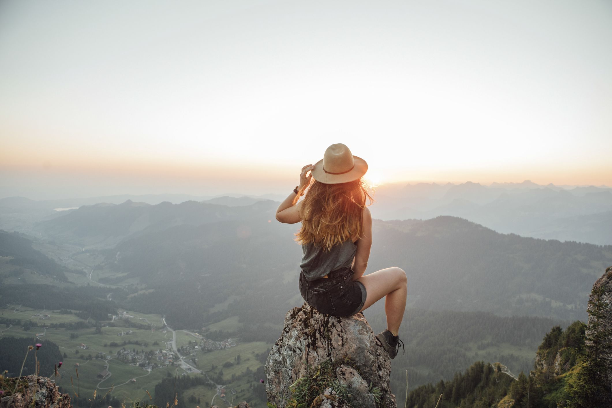 Una giovane donna è seduta su una roccia in montagna e guarda con fiducia il panorama.